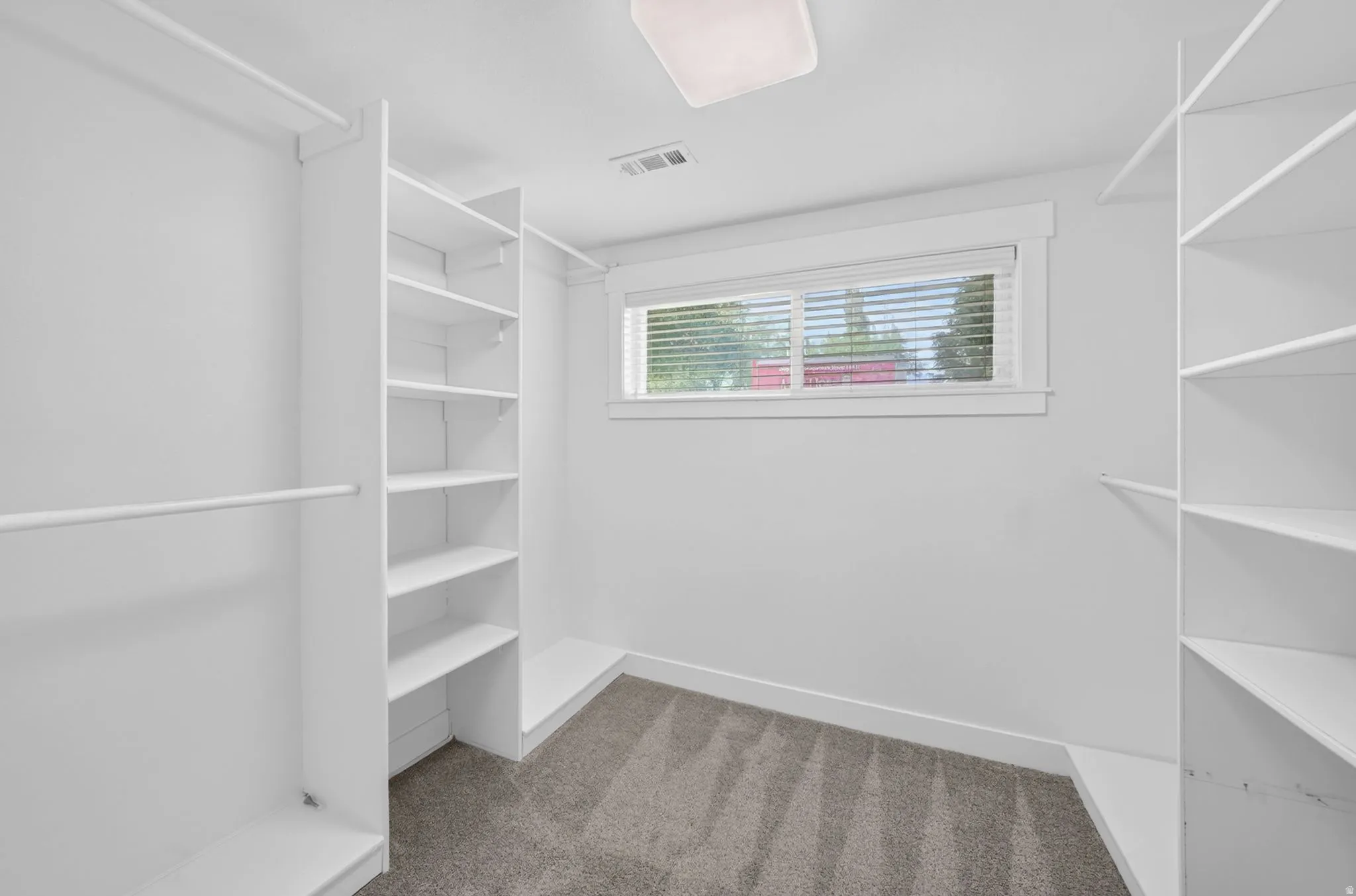 Walk-in closet featuring white built-in shelving, hanging rods, and a window with horizontal blinds