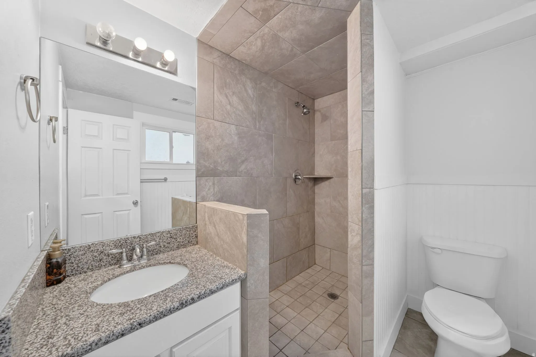 Bathroom featuring a walk-in shower with full-height tile surround, a built-in shower niche, and a tiled floor