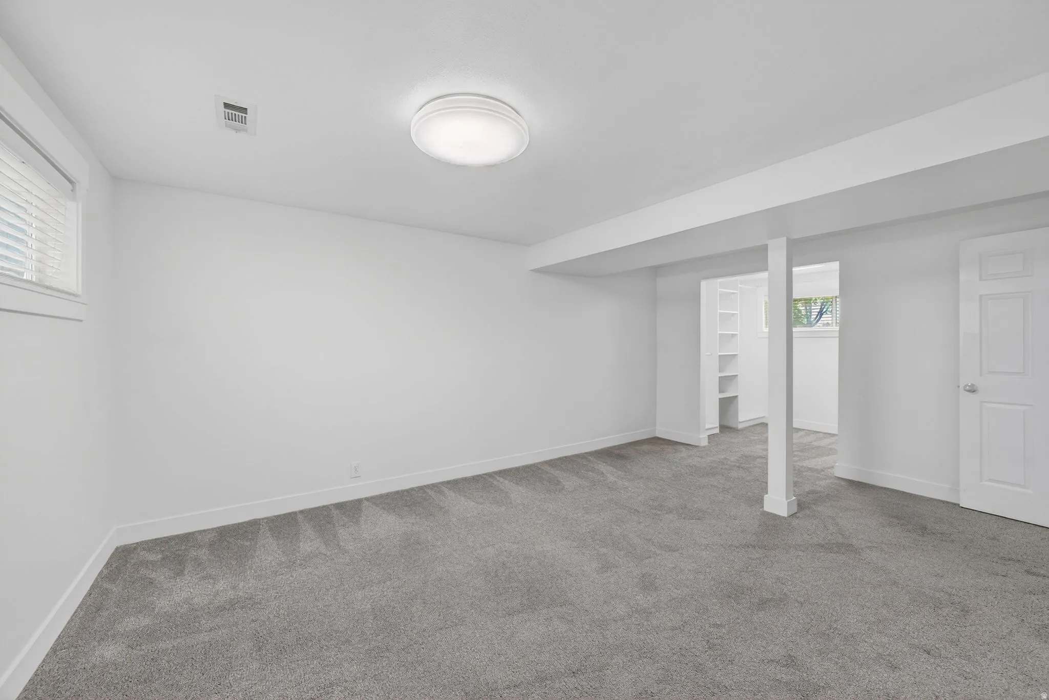 Spacious room featuring neutral carpeting, white walls, and a window with blinds