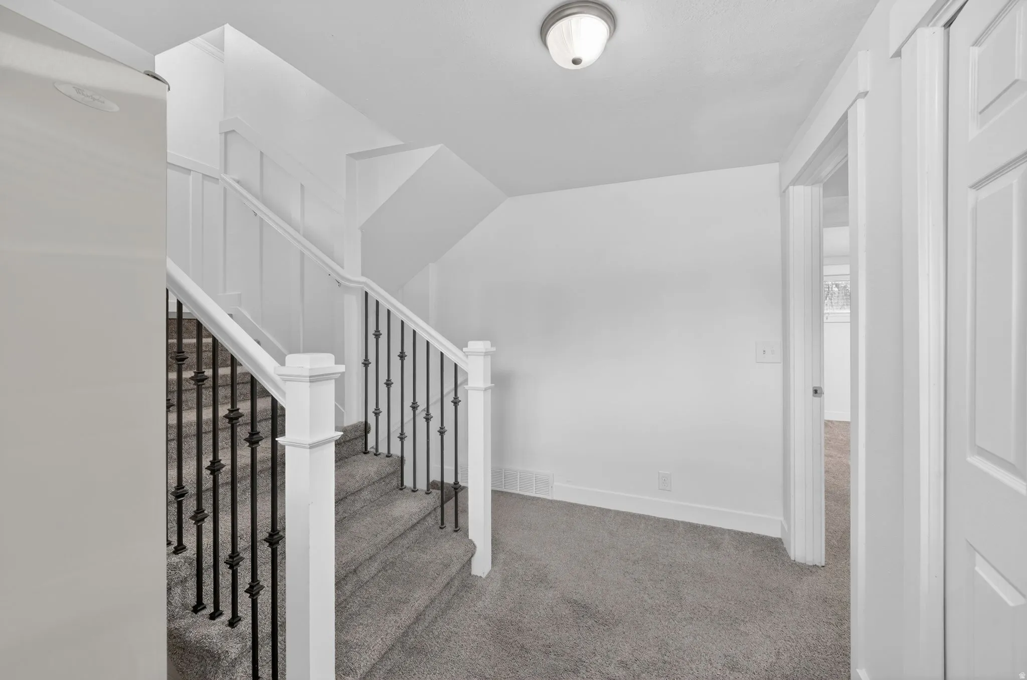 Staircase featuring white newel posts, railings, and black wrought iron balusters