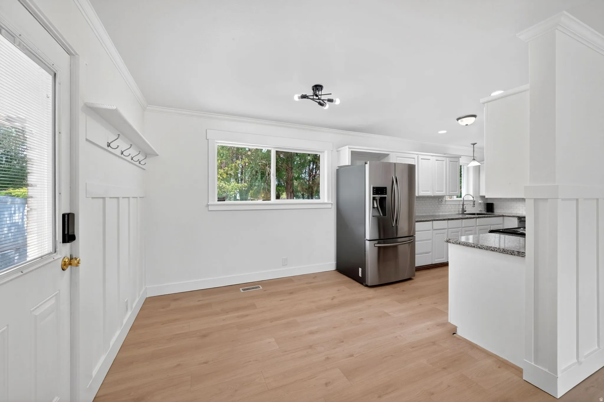 Open-concept living space featuring wood-finish flooring, white board-and-batten wall detailing, a stainless steel refrigerator, white cabinetry, and granite countertops