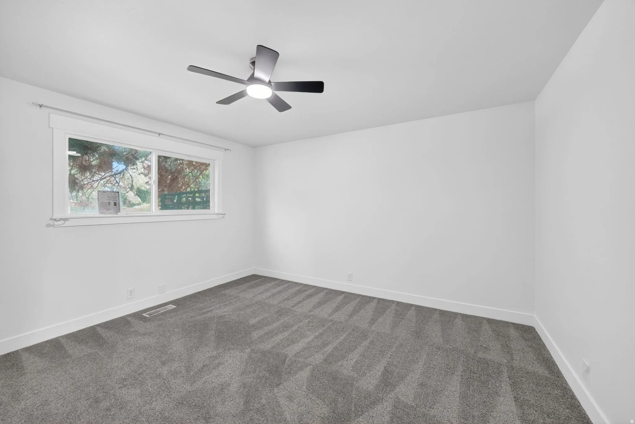 Spacious room featuring neutral carpeting, white walls, and a modern ceiling fan with integrated lighting