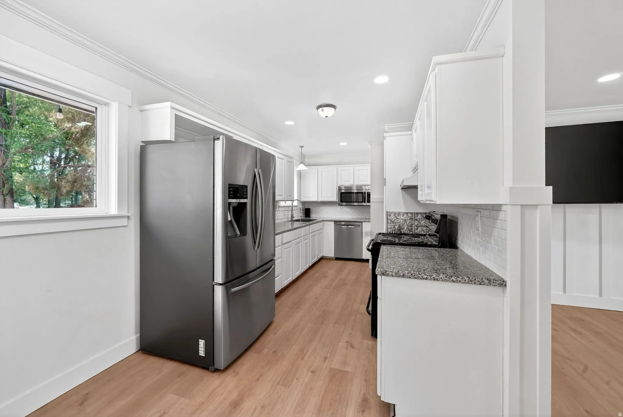 Kitchen featuring wood-finish flooring, white cabinetry, granite-patterned countertops, and a white subway tile backsplash