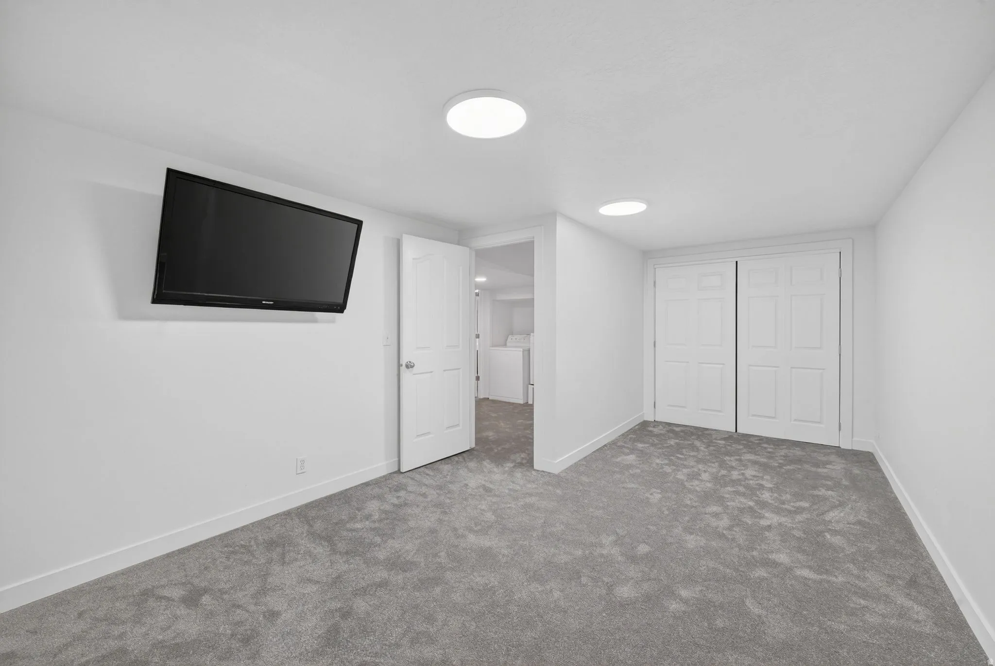 Carpeted room featuring white walls, baseboards, and ceiling, with two flush-mount ceiling lights, and two paneled bifold doors