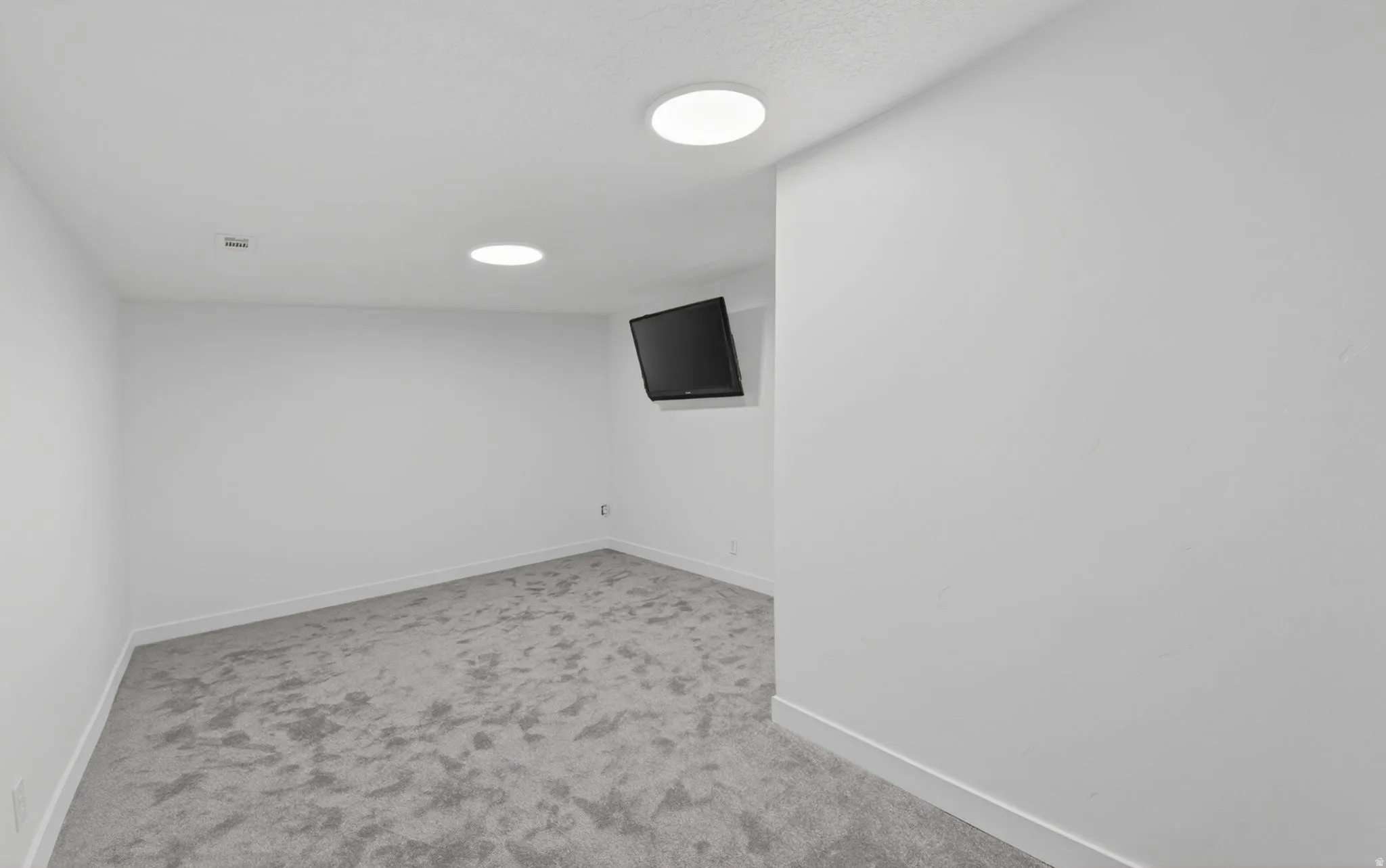 Interior room featuring plush gray carpet, white walls, white baseboards, and two recessed circular ceiling lights