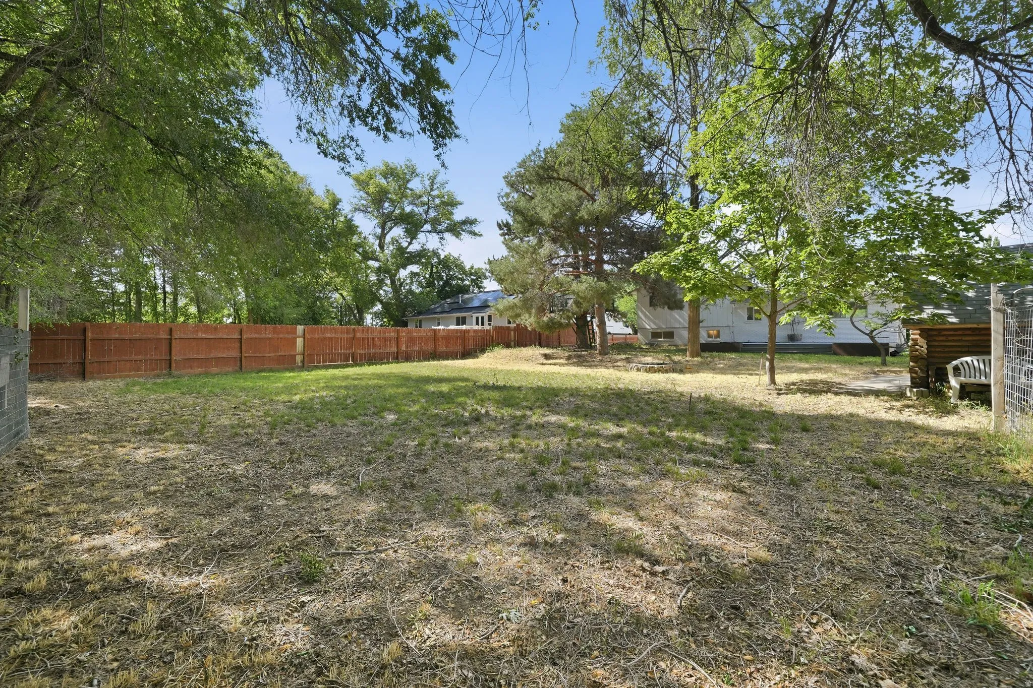 Expansive outdoor space featuring a full perimeter privacy fence, mature trees providing natural shade, and a substantial grassy area