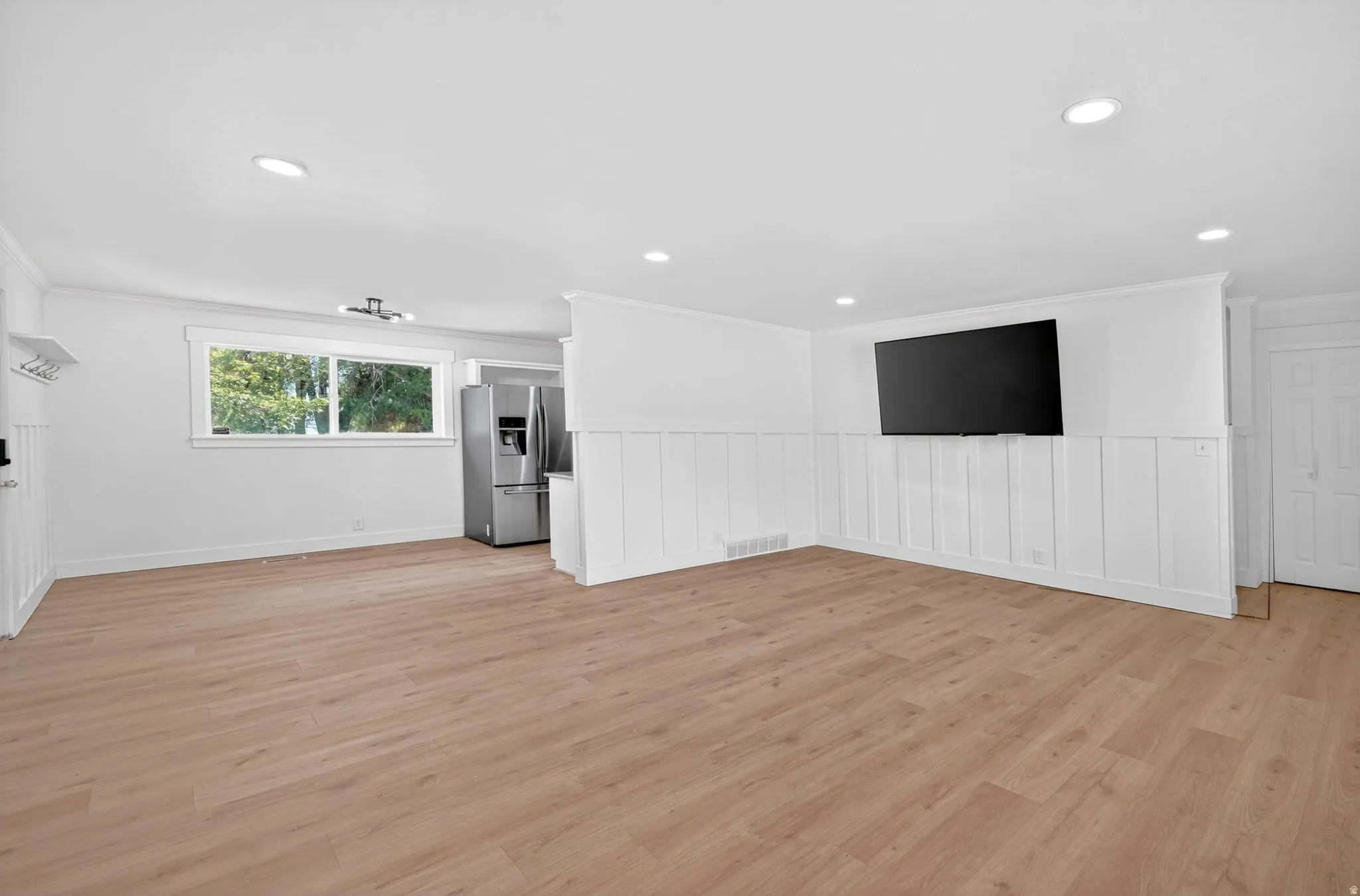 Spacious area featuring light wood-finish flooring, recessed lighting, and white wainscoting
