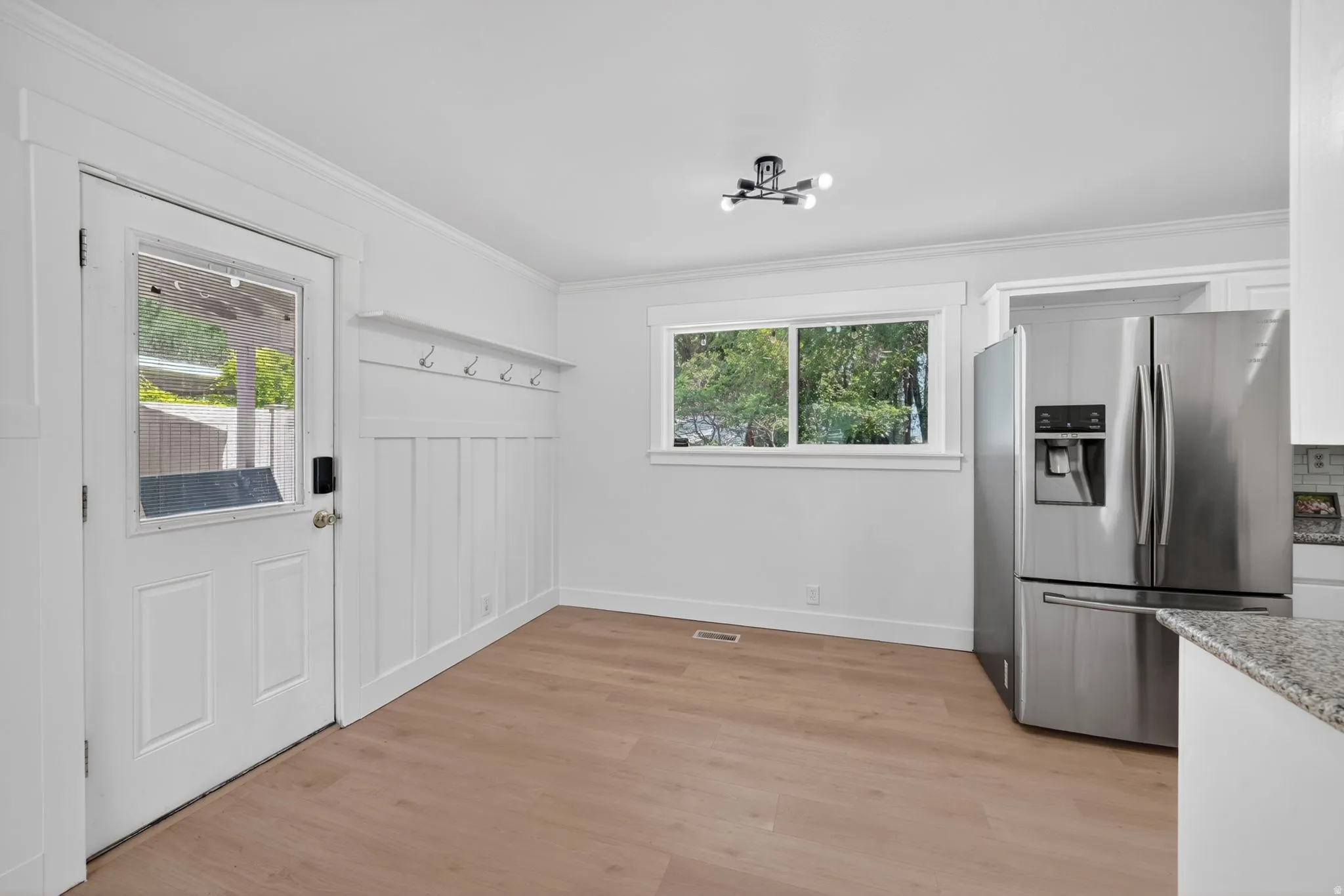 Bright interior space featuring wood-finish flooring, a contemporary ceiling light fixture, and a stainless steel refrigerator