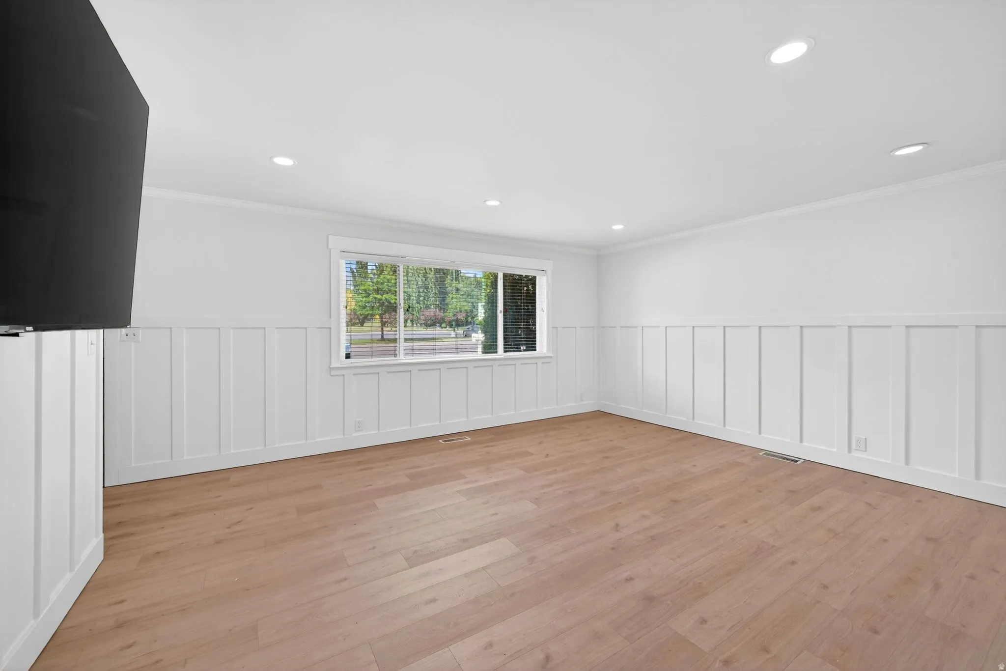 Spacious room featuring wood-finish flooring, white board and batten wall paneling, recessed lighting, and a large window