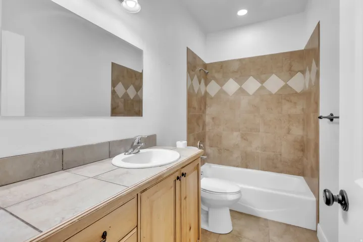 Bathroom featuring a light wood-finish vanity with a tile countertop, a white drop-in sink, and a large wall-mounted mirror