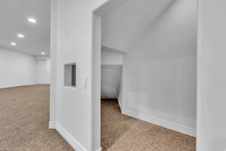 Carpeted under-stair storage area with white baseboards and light neutral wall paint