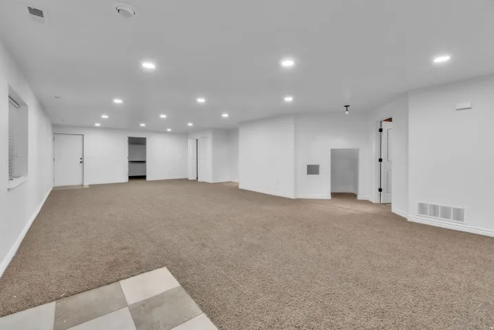 Expansive carpeted area featuring recessed lighting, white walls, and multiple access points