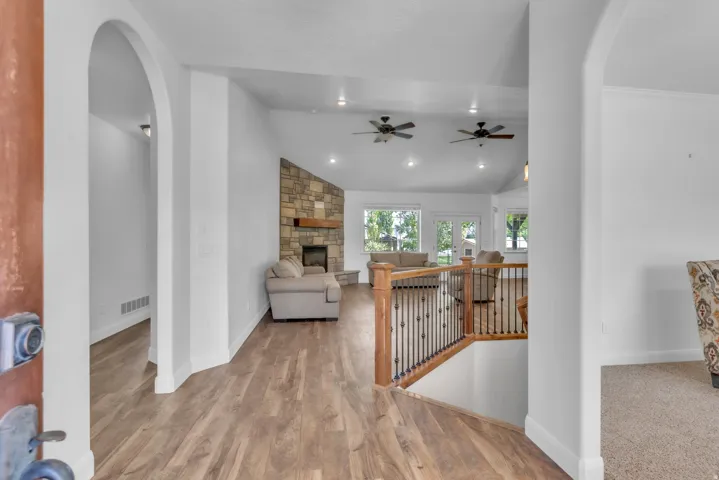Expansive living space featuring wood-finish flooring, a stone fireplace with a wood mantle, vaulted ceilings, recessed lighting, and multiple ceiling fans