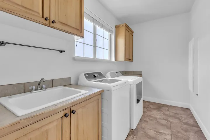 Dedicated laundry area featuring a utility sink set into a tiled countertop with wood-finish cabinetry