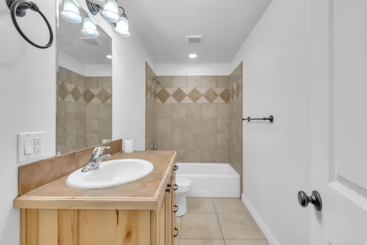 Bathroom featuring a light wood vanity with a drop-in sink, tiled countertop, and matching tiled backsplash