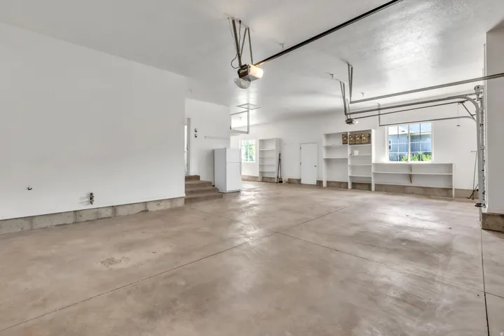 Spacious garage featuring a concrete floor, built-in shelving, two garage door openers, and a window for natural light
