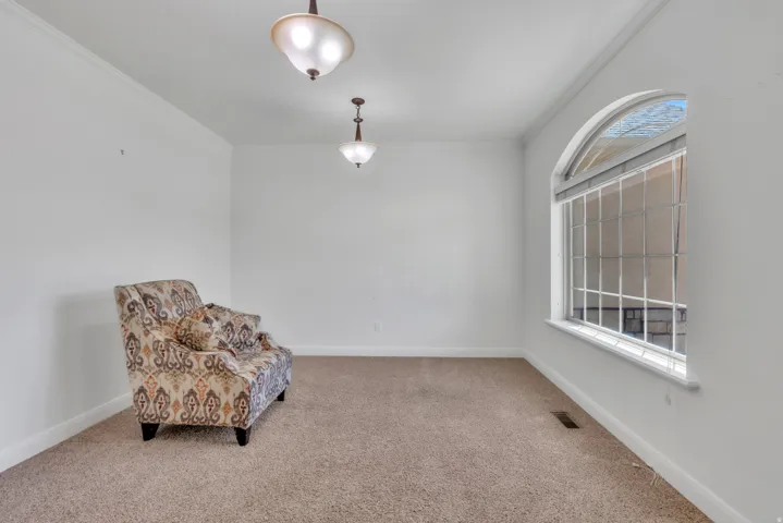 Light-filled interior space featuring a large arched window with grid details, crown molding, two ceiling-mounted light fixtures, and neutral carpeting