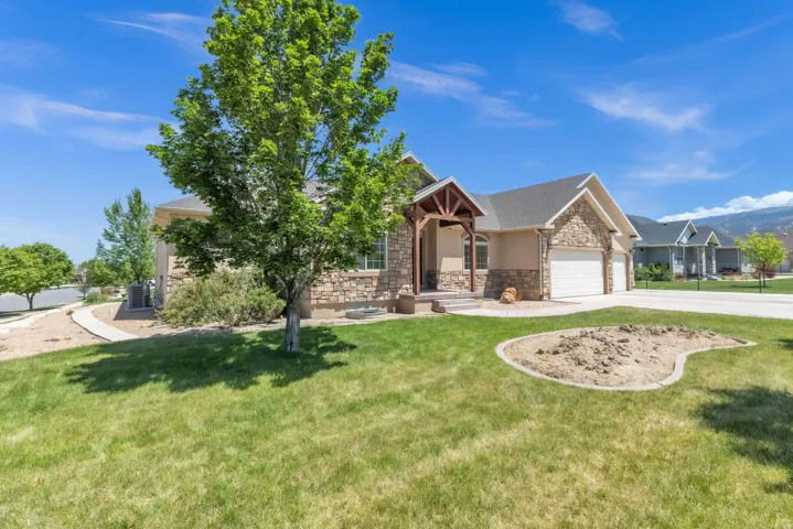 Stucco and stone exterior featuring a covered entry with wood beams, a two-car garage, and established landscaping