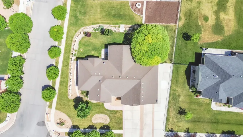 Spacious corner lot featuring a multi-gabled roofline, extensive paved driveway, mature landscaping, and a manicured lawn