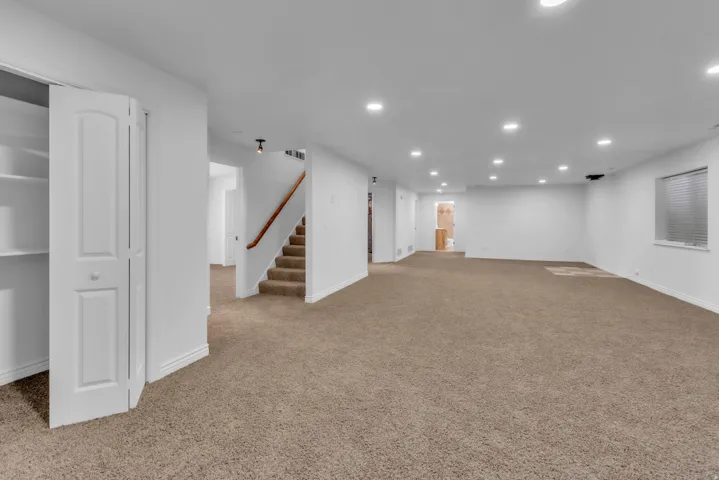 Spacious lower-level room featuring plush carpeting, recessed lighting, and a window with blinds