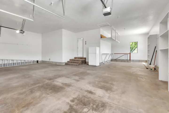 Spacious garage featuring a concrete floor, built-in shelving, elevated storage, and a large window providing natural illumination
