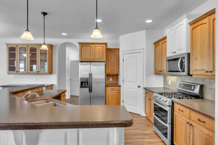 Kitchen featuring stainless steel appliances, wood-finish cabinetry, neutral countertops, a tile backsplash, and recessed and pendant lighting