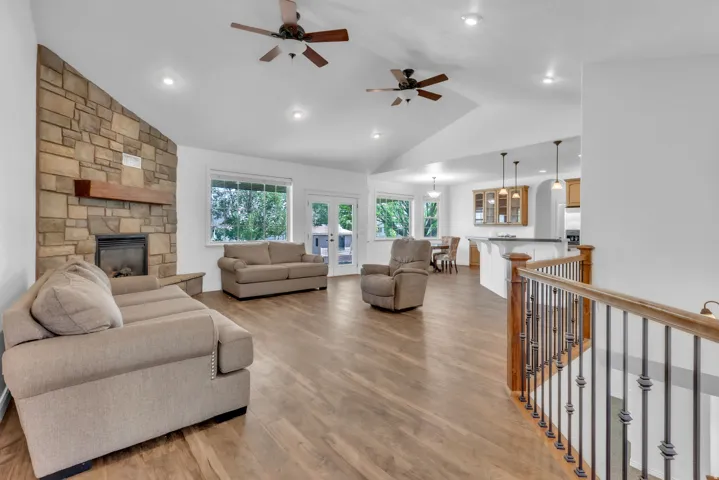 Spacious living area featuring a stone-clad fireplace with wood mantel, vaulted ceilings with recessed lighting, wood-finish flooring, and French doors