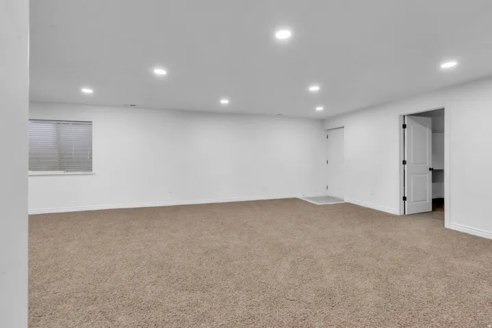 Spacious room featuring neutral carpet flooring, recessed lighting, white walls, a window with horizontal blinds, and a white interior door