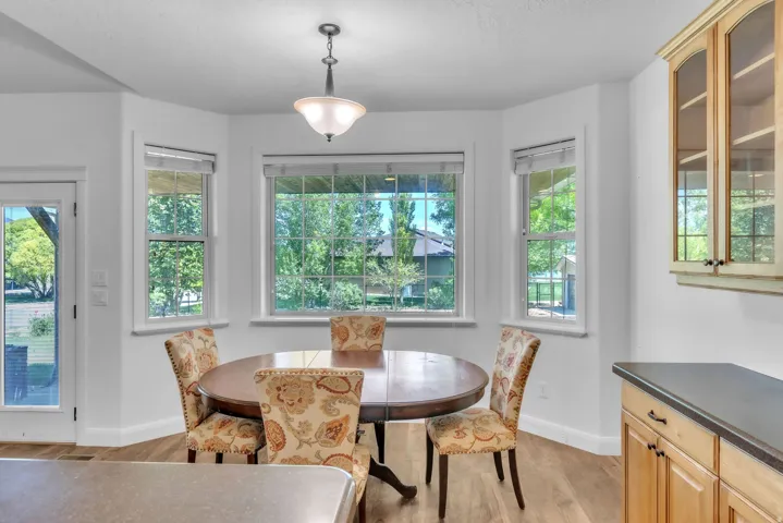 Breakfast nook featuring bay windows, wood-finish flooring, a glass-paneled patio door, a hanging light fixture, and built-in cabinetry with glass inserts and dark countertops