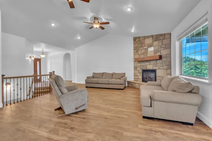 Spacious living area featuring wood-finish flooring, a stone-accented fireplace with a wood mantle, and a large window