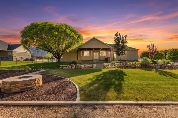 Exterior featuring a covered porch with exposed beams, a manicured lawn, a built-in stone fire pit, and mature trees