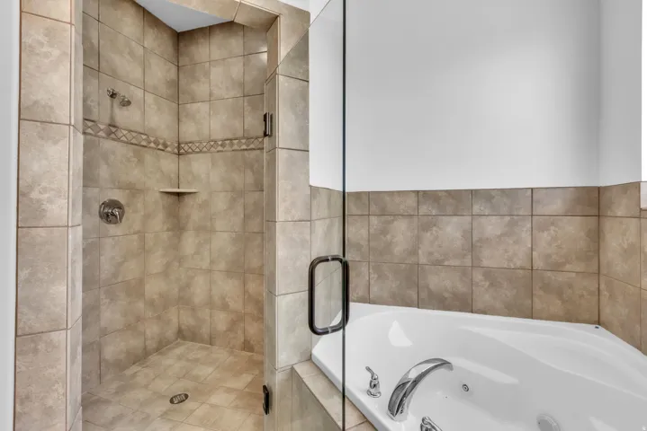 Tiled shower with glass enclosure featuring a decorative accent band and integrated corner shelf