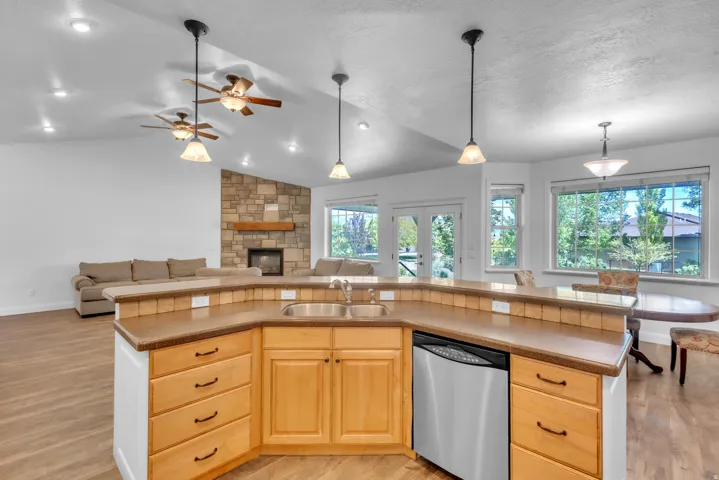 Kitchen island with light wood cabinetry, a stainless steel dishwasher, and a double basin sink, featuring pendant lighting and wood-finish flooring