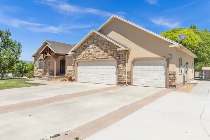 Exterior featuring a stucco and stone facade, covered entry porch, two attached garage doors, and a concrete driveway with decorative banding