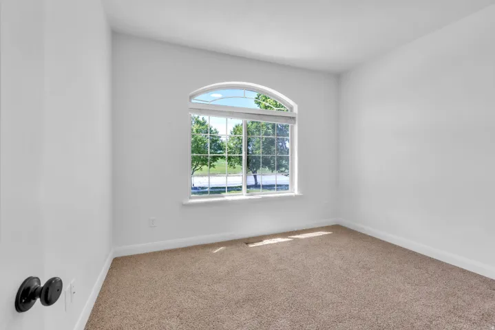 Light-filled room featuring an arched window with grid panes, white walls, and neutral carpet flooring