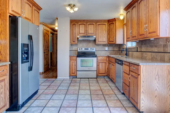Kitchen featuring wood cabinetry, stainless steel appliances, tile flooring, and a tile backsplash