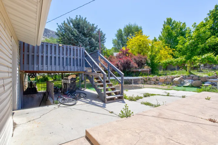 Rear exterior featuring a raised wooden deck with staircase access, concrete patio, and mature landscaping