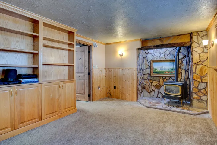 Built-in shelving with lower cabinetry, stone-clad fireplace with hearth, wood-finish paneling, and wall sconces