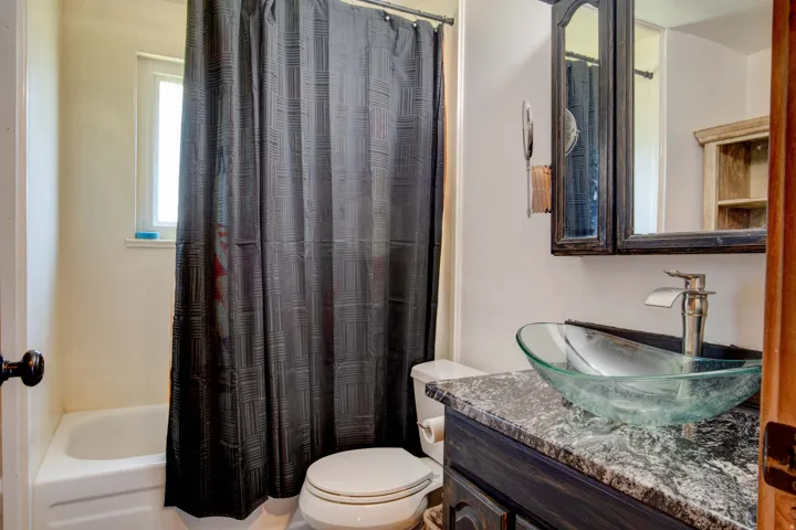 Bathroom featuring a glass vessel sink, dark wood vanity with a stone-look countertop, a bathtub, and a window
