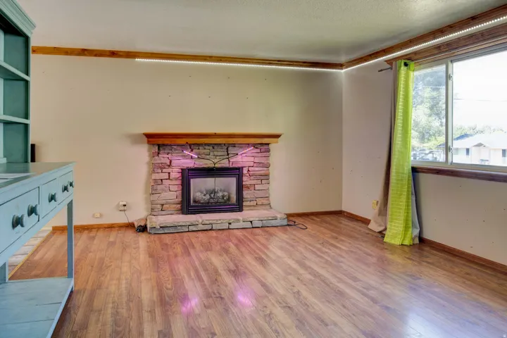Wood-finish flooring, stone-clad fireplace with wood mantle, built-in shelving, and large window