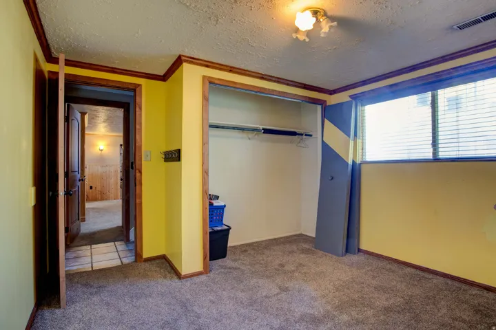 Carpeted room featuring a window with blinds, an open closet with a hanging rod, and wood-finish trim around doorways and the ceiling