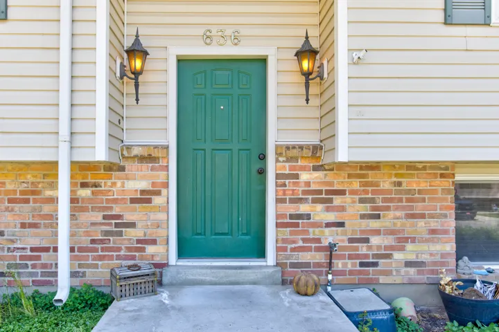 Green paneled entry door with house numbers 636, flanked by two exterior wall sconces