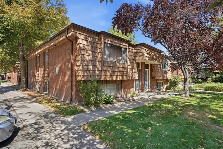 Brick and shingle exterior with a prominent entry, mature trees, and a paved walkway