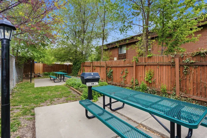 Outdoor communal area featuring a wood privacy fence, concrete patios, green picnic tables, and a built-in gas grill