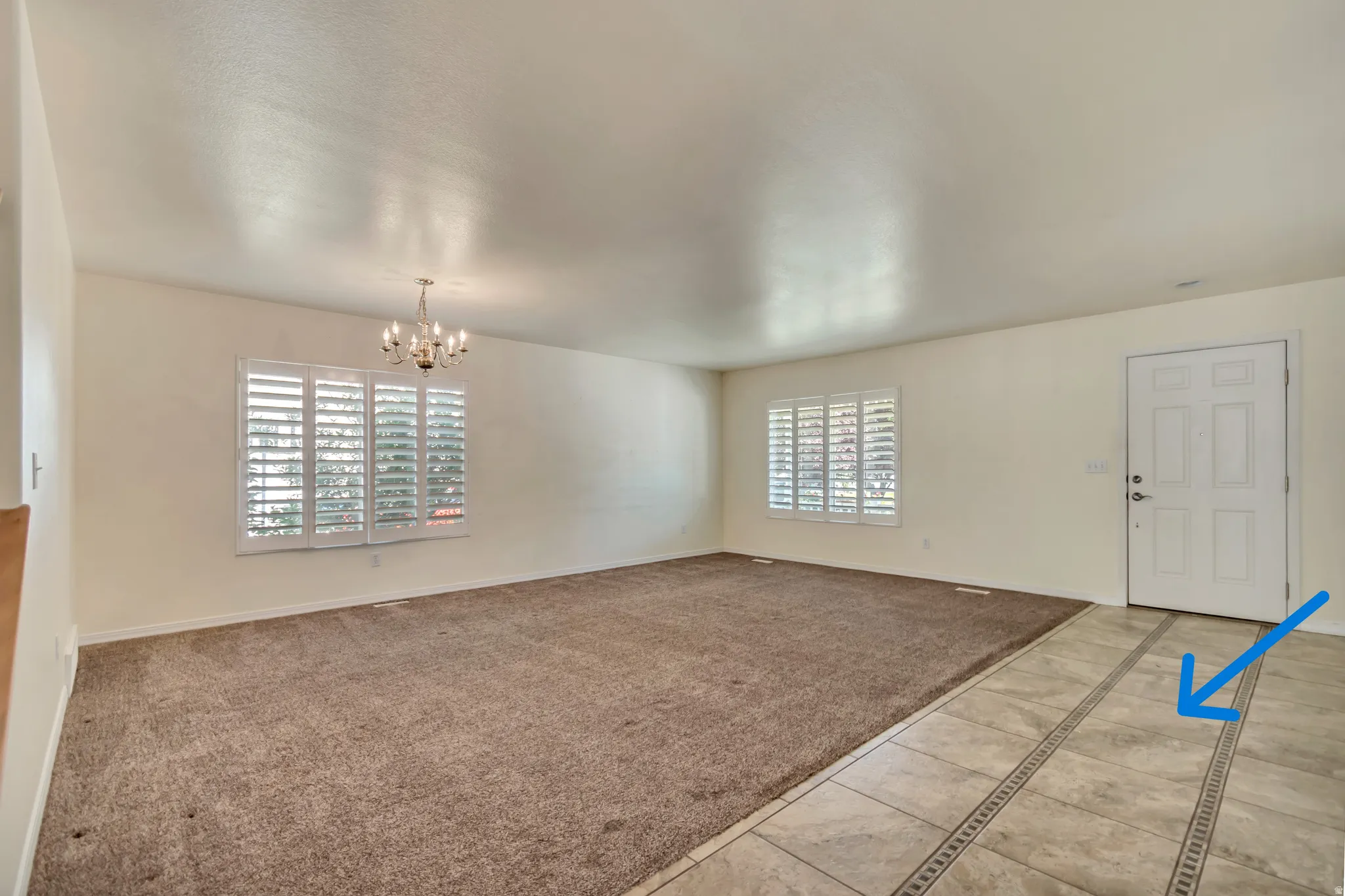 Spacious living area featuring neutral carpeting, a custom tile entry with decorative inlay(blue arrow), and