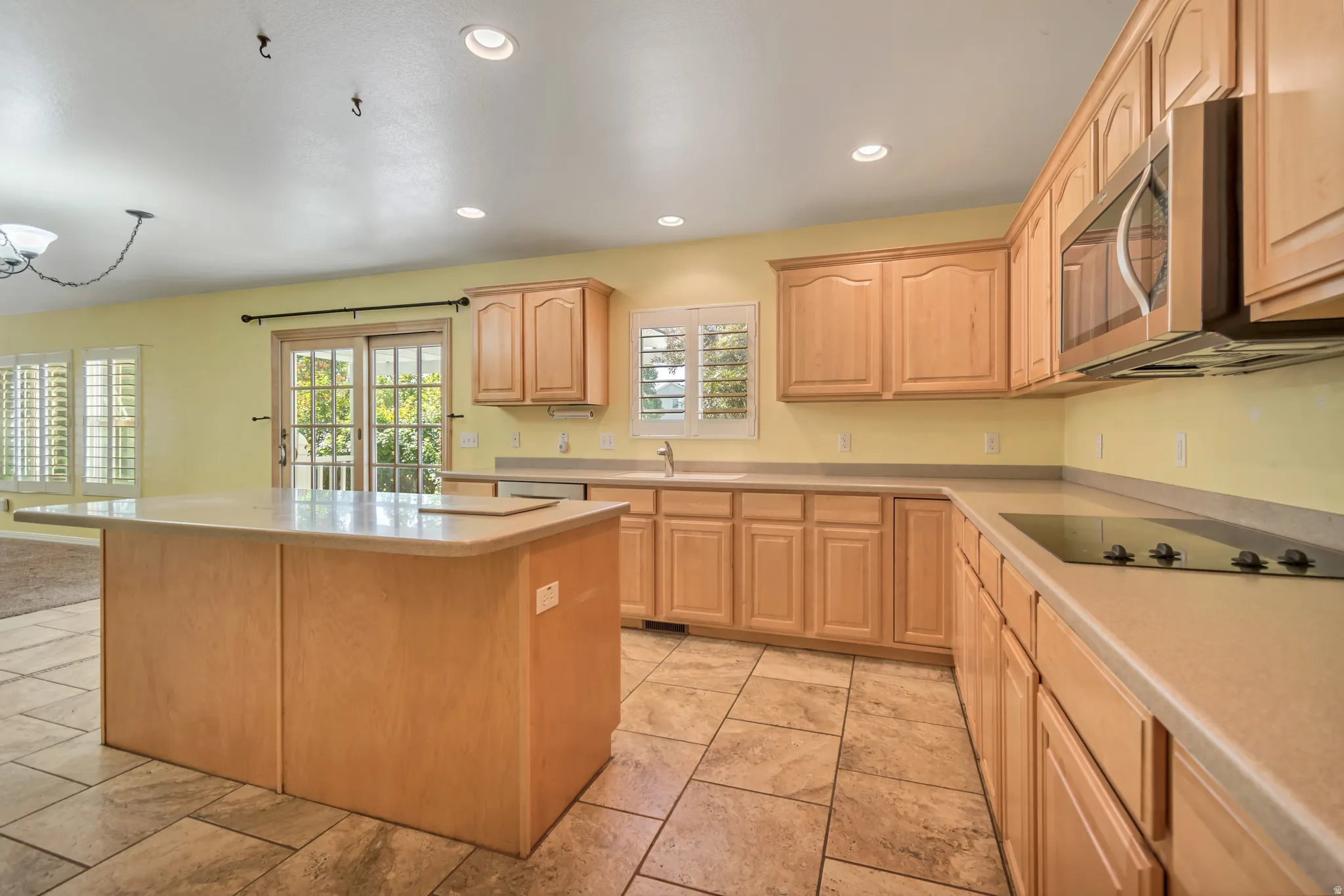Open-concept kitchen featuring an island with countertop seating, wood-finish cabinetry, tile flooring, and sliding glass door