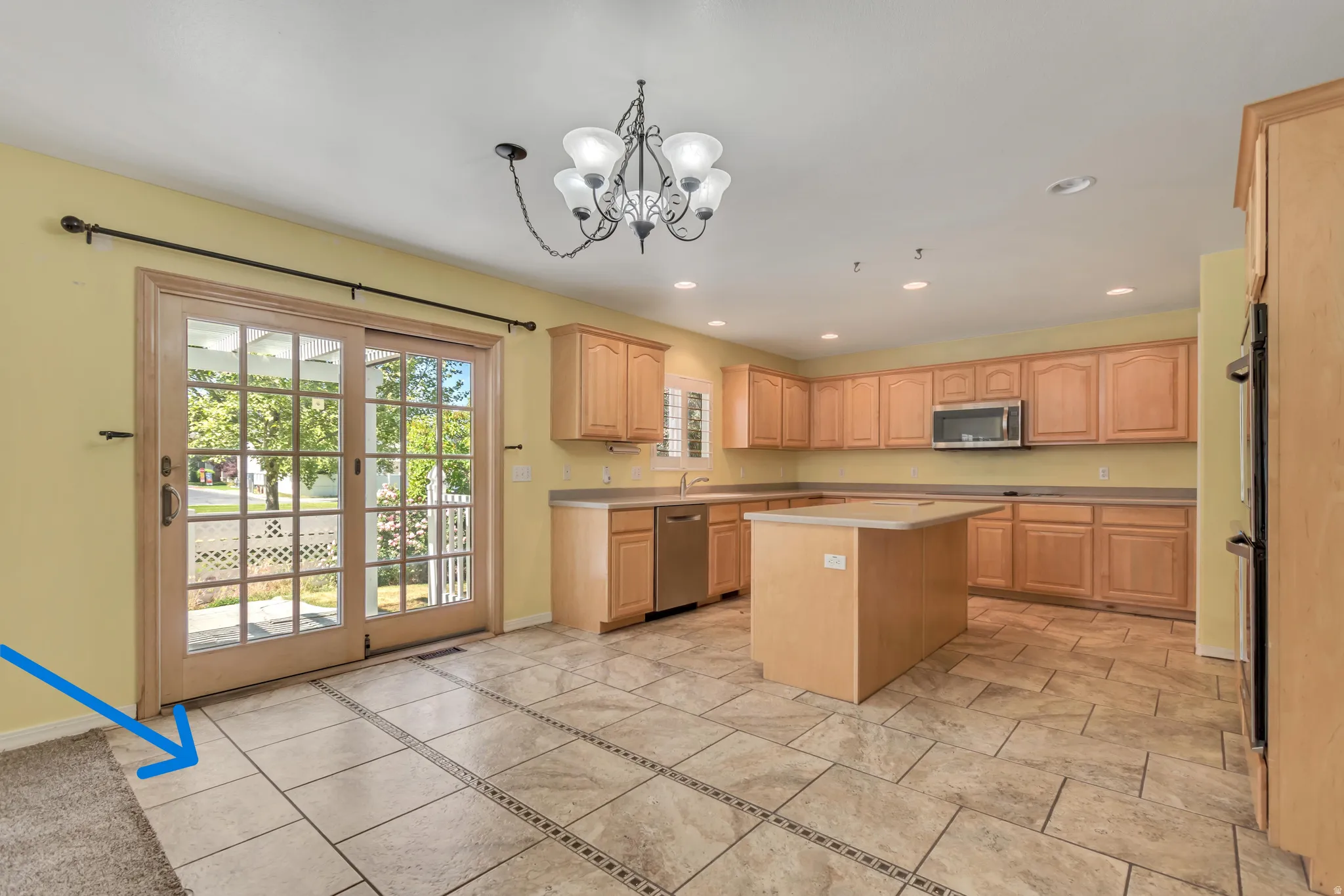 Kitchen featuring extensive light wood cabinetry, a central island, stainless steel appliances, and custom tile (blue arrow) with decorative inlay