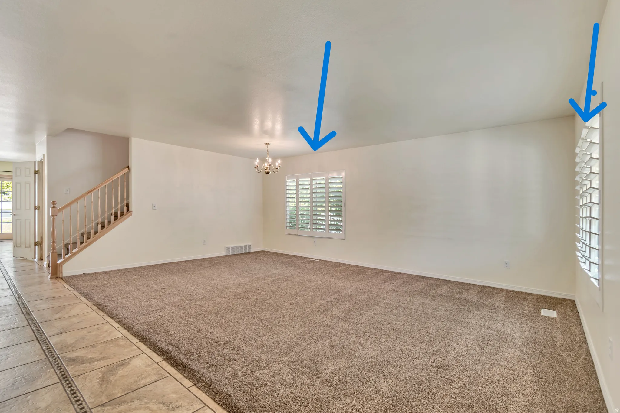 Spacious room featuring neutral carpeting, white walls, and multiple windows with white plantation shutters