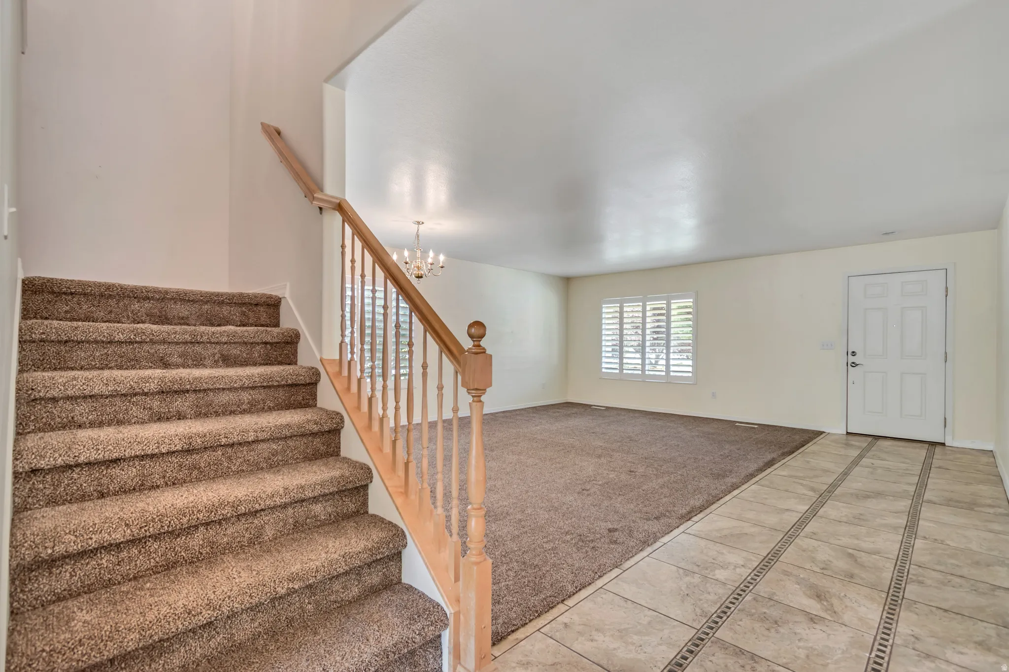 Entryway featuring tiled flooring with decorative inlays, a white paneled front door, and a carpeted staircase with a wood railing