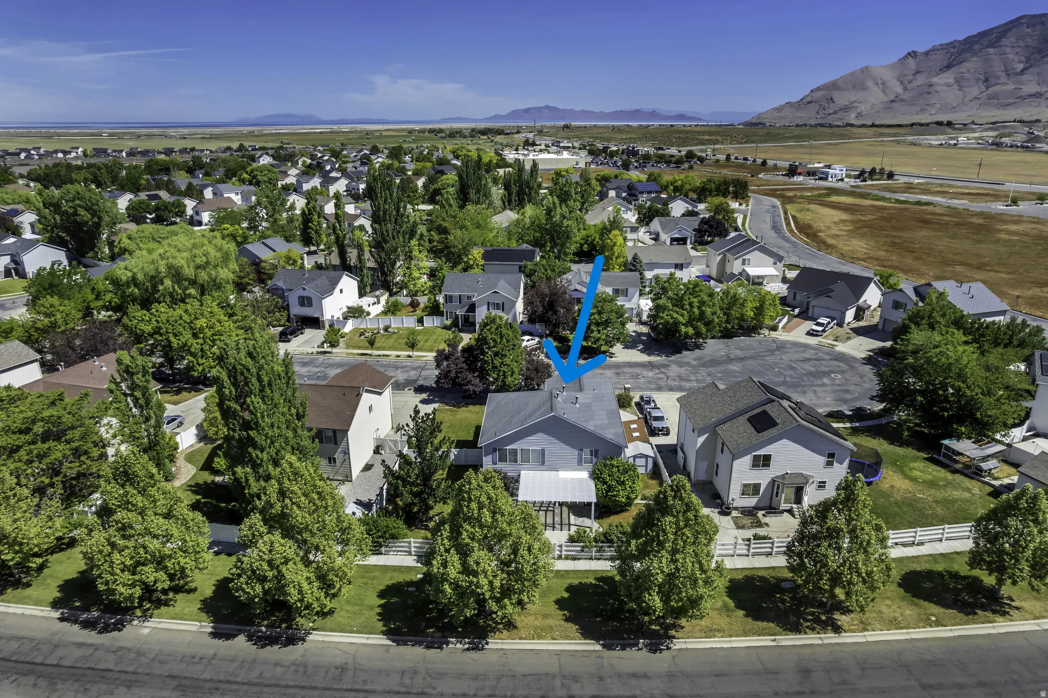 Residential property in a neighborhood setting with established trees and surrounding mountainous terrain (blue arrow)